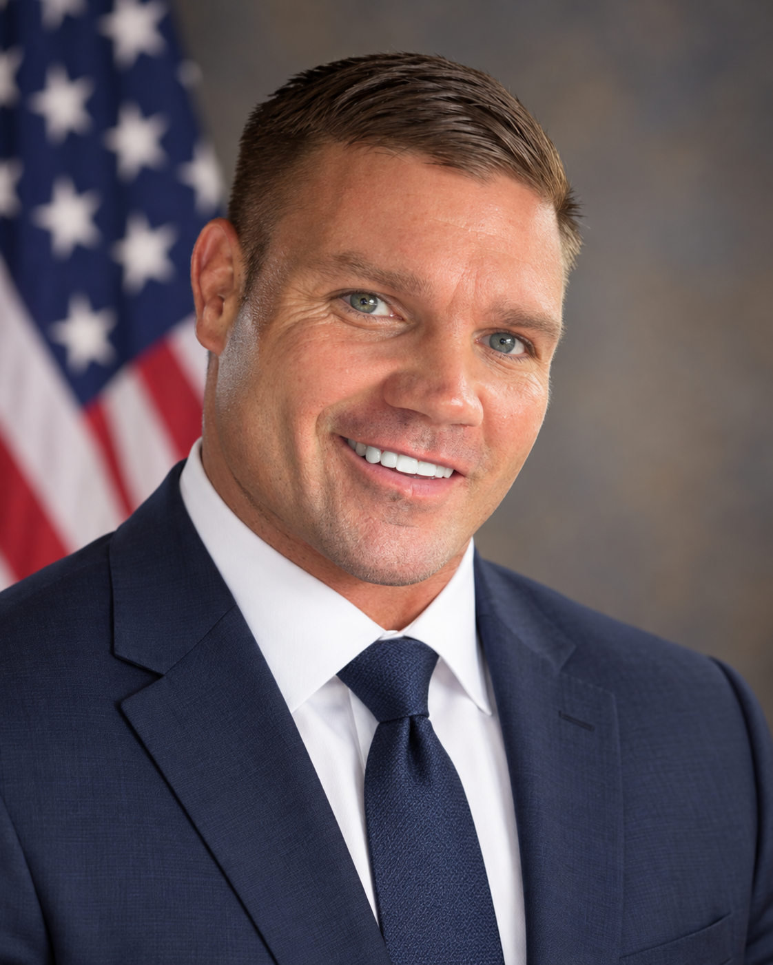Jonathan Gallogly in a navy suit with an American flag behind him